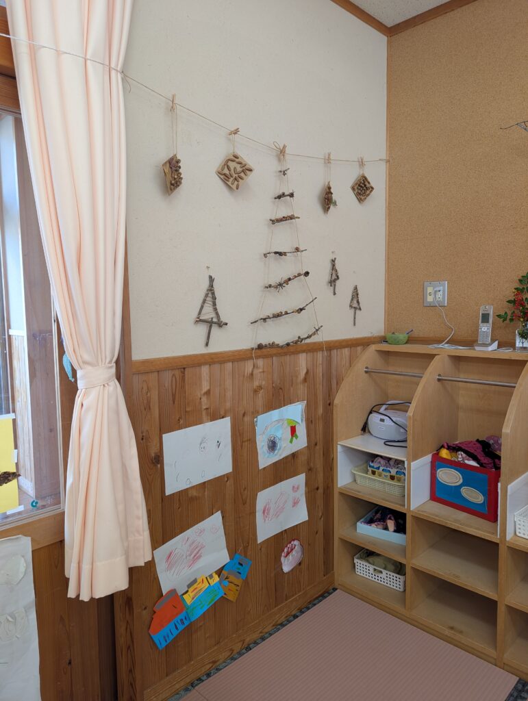 園舎の壁面。麻紐に木の実で作ったクリスマスツリーのようなオーナメントが吊るされ、その下には子どもたちが自由に描いた絵が飾られている。